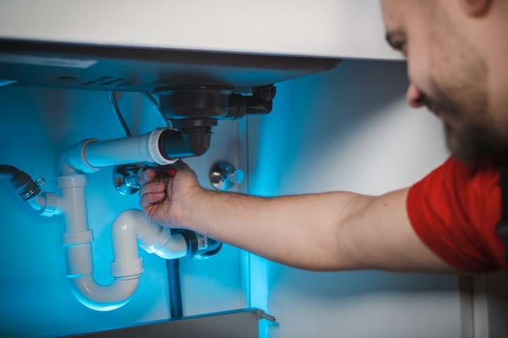 Plumber working on pipes under a sink